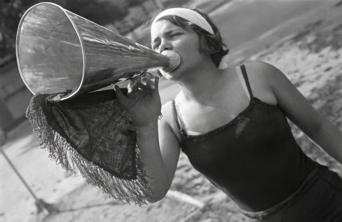 Žena vo vintage štýle kričí do megafónu vonku; čiernobiela fotografia s retro atmosférou.