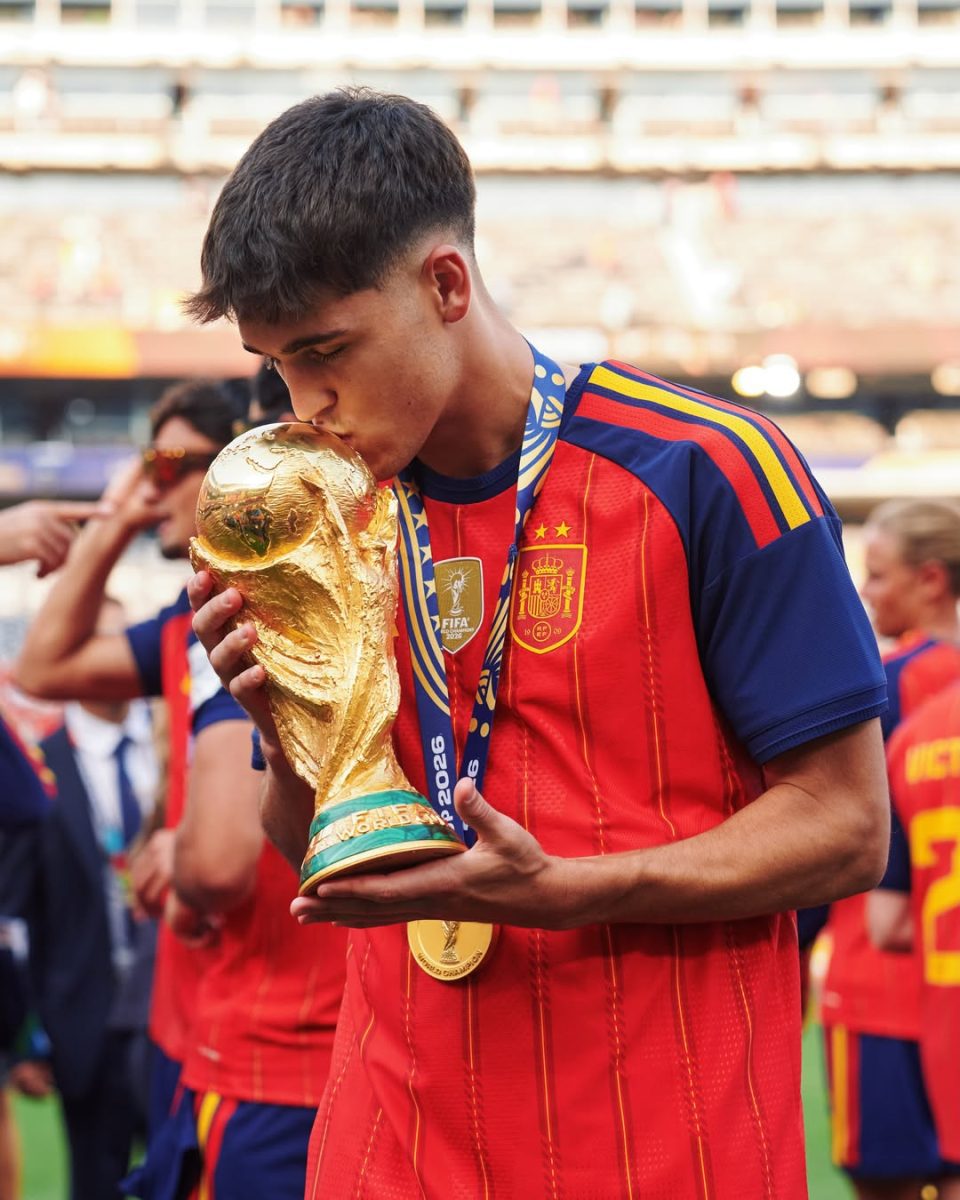Futbalista v španielskom drese bozkáva trofej majstrovstiev sveta na štadióne.