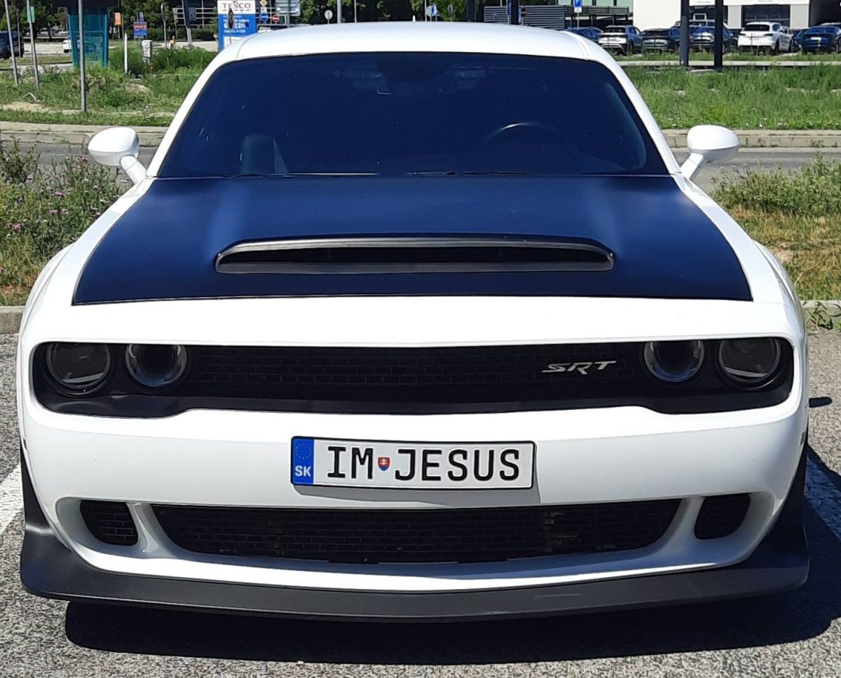 Biely športový automobil SRT s čiernou kapotou a poznávacou značkou IM JESUS na parkovisku.