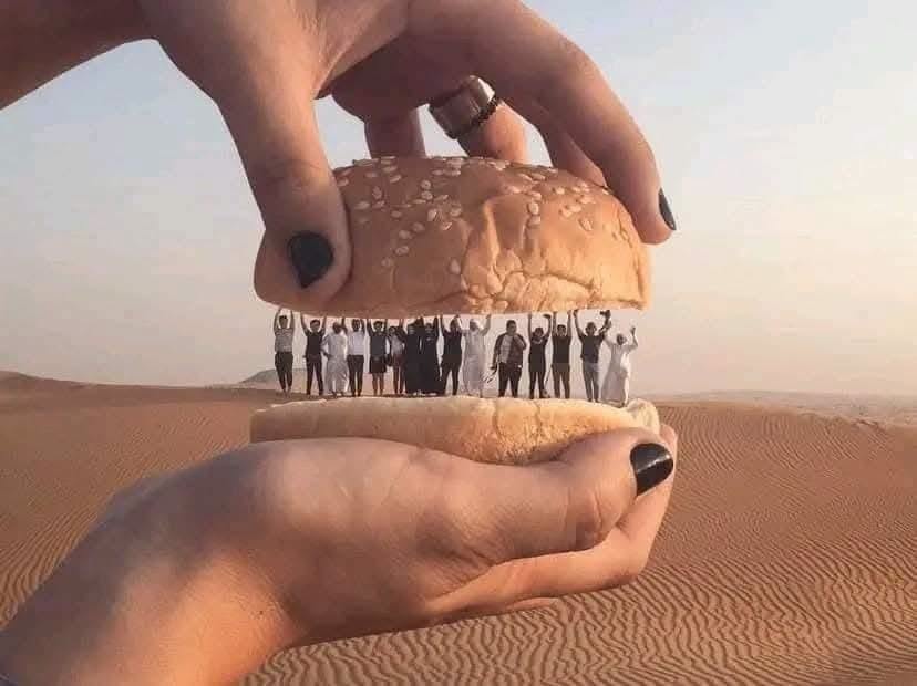 Osoby v púšti medzi obrovskými žemľami, iluzórny hamburger v prírode.