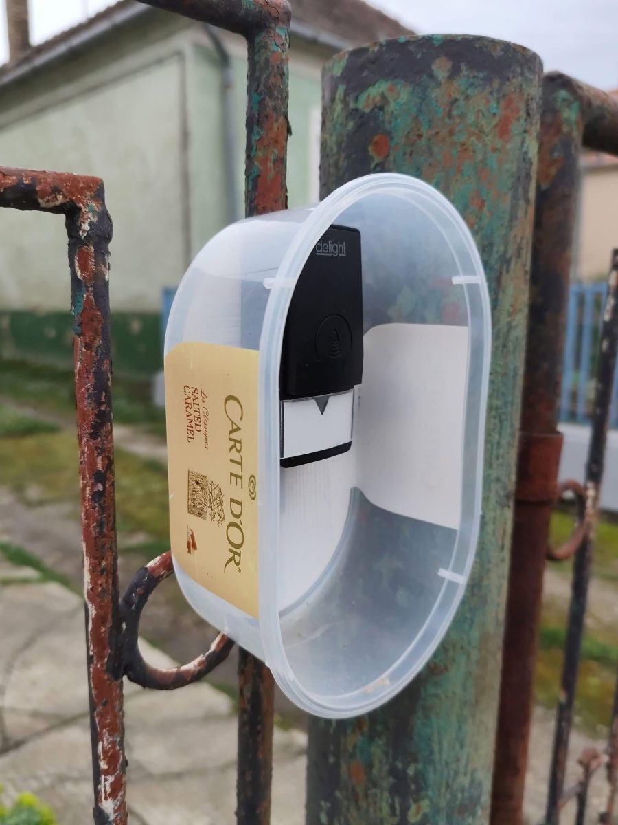 Plastová nádoba na zmrzlinu použitá ako držiak na bráne so zvončekom, kreatívne použitie recyklovaného materiálu.