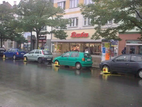 Autá na ulici s nasadenými papučami, parkovanie pred obchodom počas daždivého dňa, Bratislava.