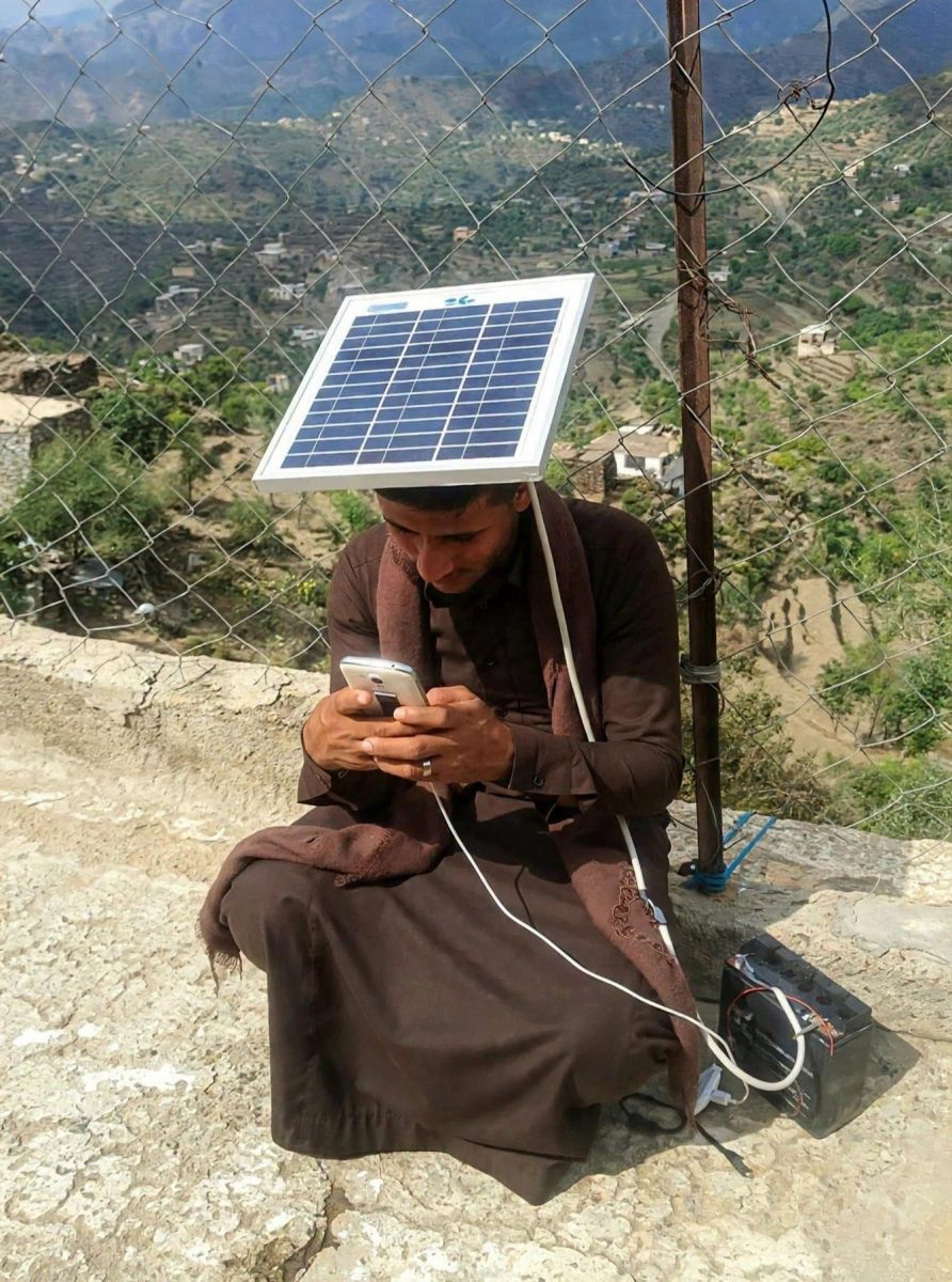 Muž so solárnym panelom a mobilom nabíjaným na vidieku. Inovatívne riešenie pre nedostatok elektriny.