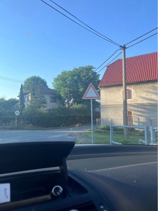 Auto zastavilo na križovatke s výstražnou dopravnou značkou v dedinského prostredí za slnečného dňa.