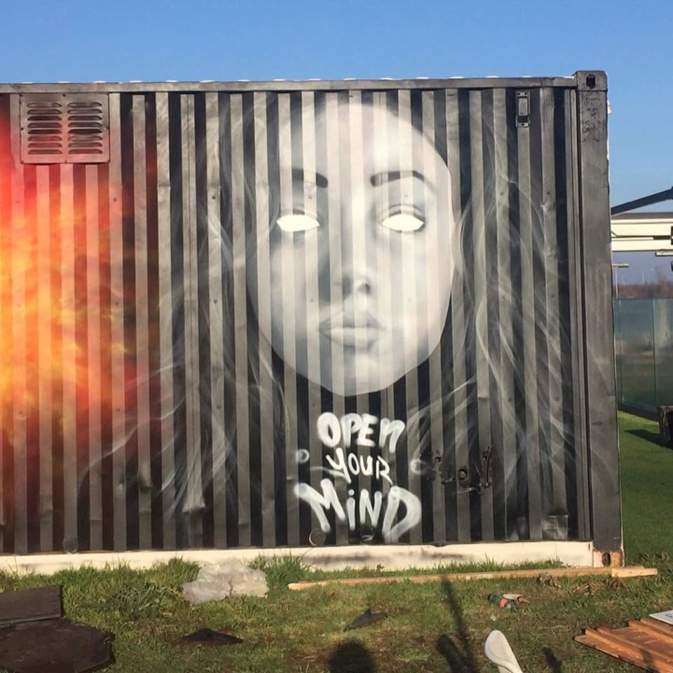 Graffiti na kontajneri: tvár ženy s bielymi očami a textom Open Your Mind.