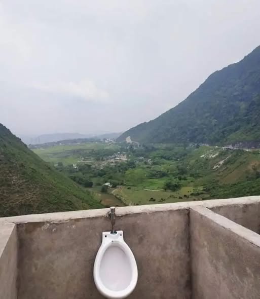 Urinal s výhľadom na malebné údolie medzi kopcami pod zamračenou oblohou.