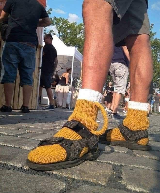 Muž v krátkych nohaviciach na ulici s originálnymi sandálmi s pletenými ponožkami počas letného festivalu.