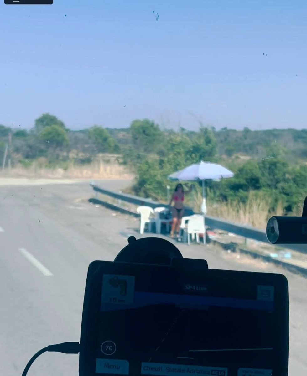 Cesta s GPS navigáciou. Žena pod slnečníkom pri kraji vozovky na vidieckej ceste počas slnečného dňa.
