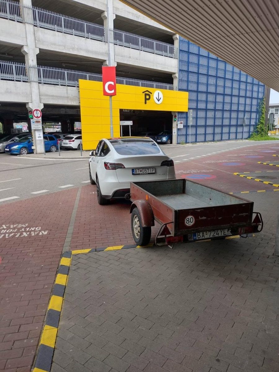 Auto s prívesným vozíkom zaparkované pri vchode do parkovacieho garáže označenej písmenom C.