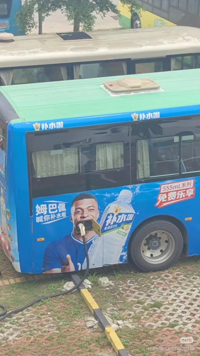 Autobus s reklamou na nápoj, nabíjanie elektrickým káblom, pripomína pitie.