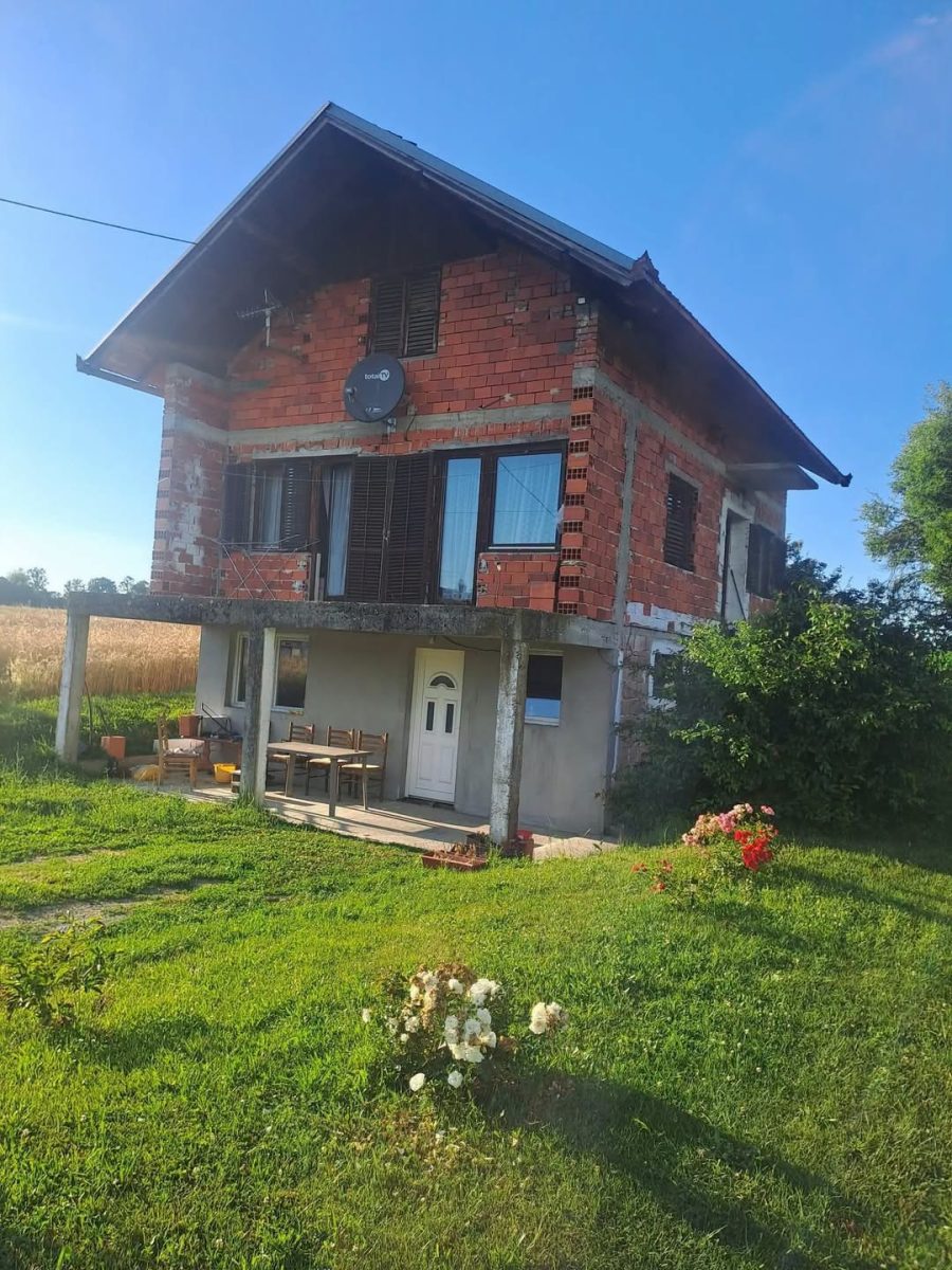 Starší vidiecky dom s tehlovou fasádou a záhradou počas slnečného dňa.