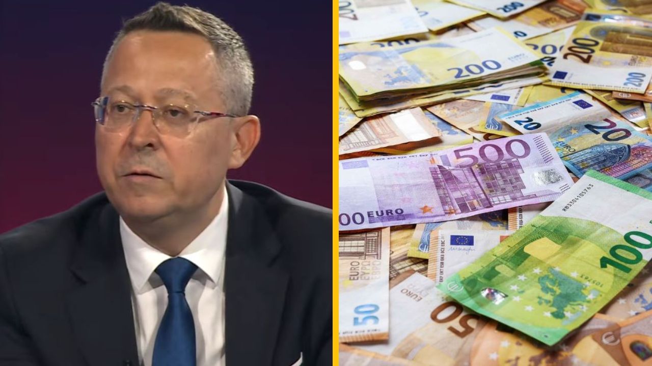 Muž v obleku s vážnym výrazom vedľa stola plného eurobankoviek.