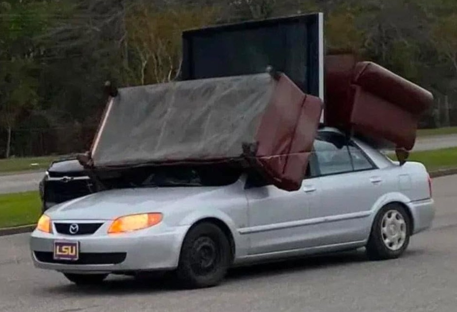 Auto nesúce veľkú pohovku na streche, neštandardný spôsob prepravy nábytku, riziko na ceste.