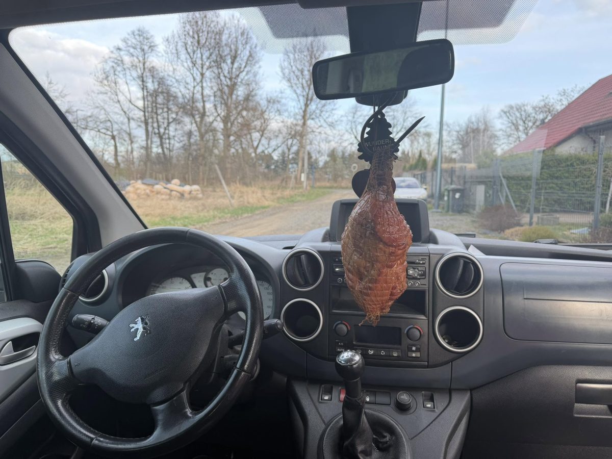 Šunka visiaca z vnútorného spätného zrkadla v aute značky Peugeot s viditeľnou palubnou doskou.