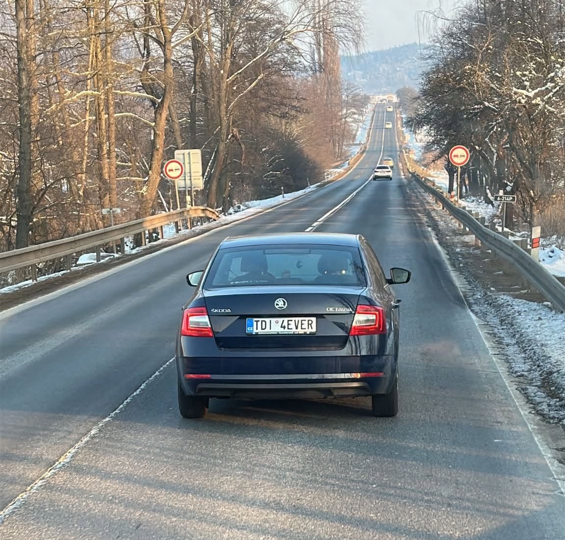 Auto Škoda Octavia na zasneženej ceste mimo mesta v zime. Dopravné značky a zimná krajina v pozadí.