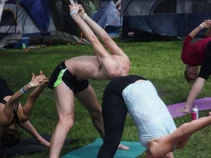 Skupina ľudí cvičí jogu pri stanoch na tráve v rámci outdoorového cvičenia.