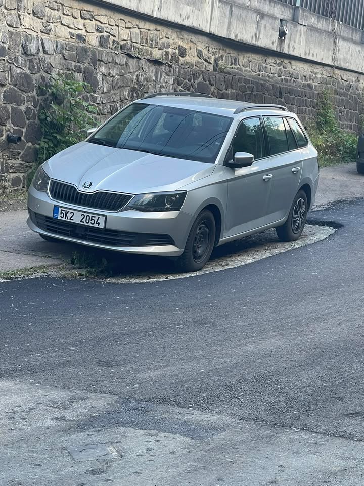 Šedé auto zaparkované na okraji cesty v blízkosti kamennej steny.
