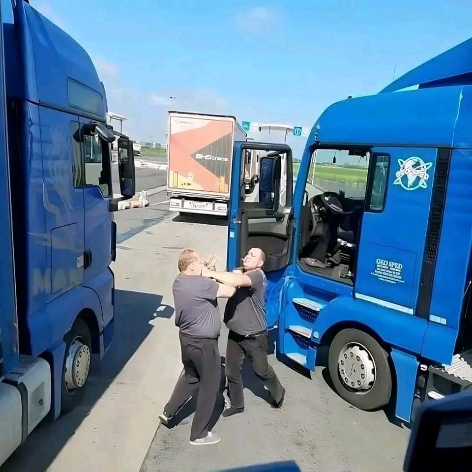 Dvaja muži sa bijú medzi modrými kamiónmi na parkovisku.