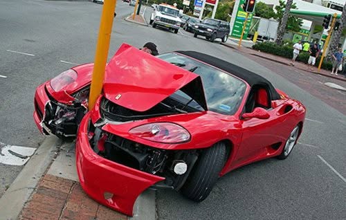 Červené športové auto nabúralo do pouličnej lampy na križovatke, poškodená predná časť vozidla.