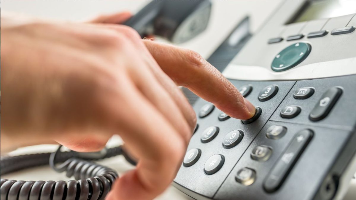 Osoba vytáča číslo na kancelárskom stolnom telefóne.