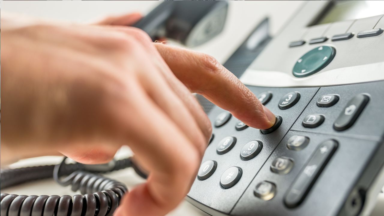 Osoba vytáča číslo na kancelárskom stolnom telefóne.