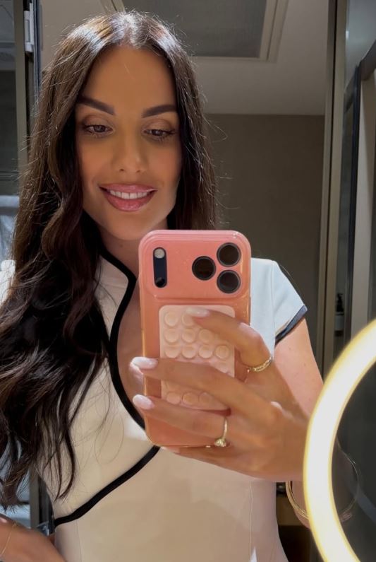 Žena so šťastným úsmevom si robí selfie v modernom prostredí, držiac telefón s ružovým púzdrom.