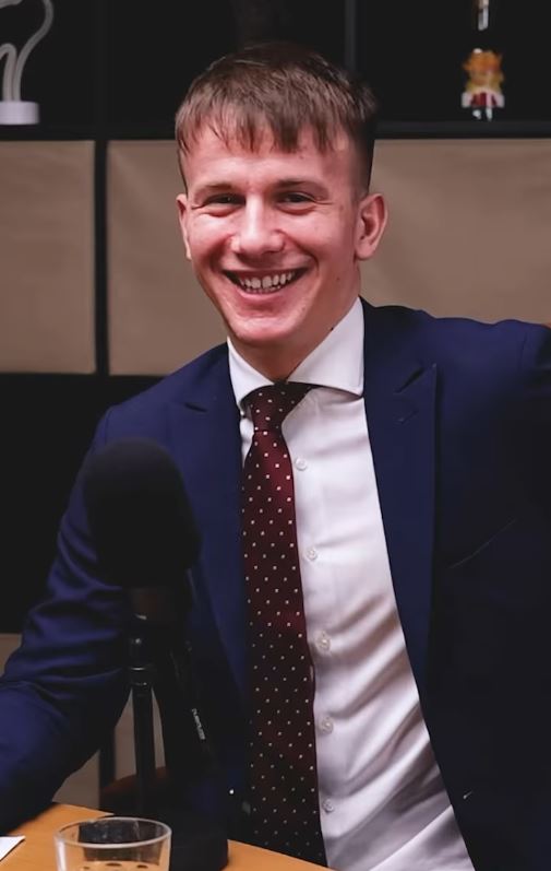 Osoba v obleku sa smeje pri mikrofóne na nahrávke podcastu.