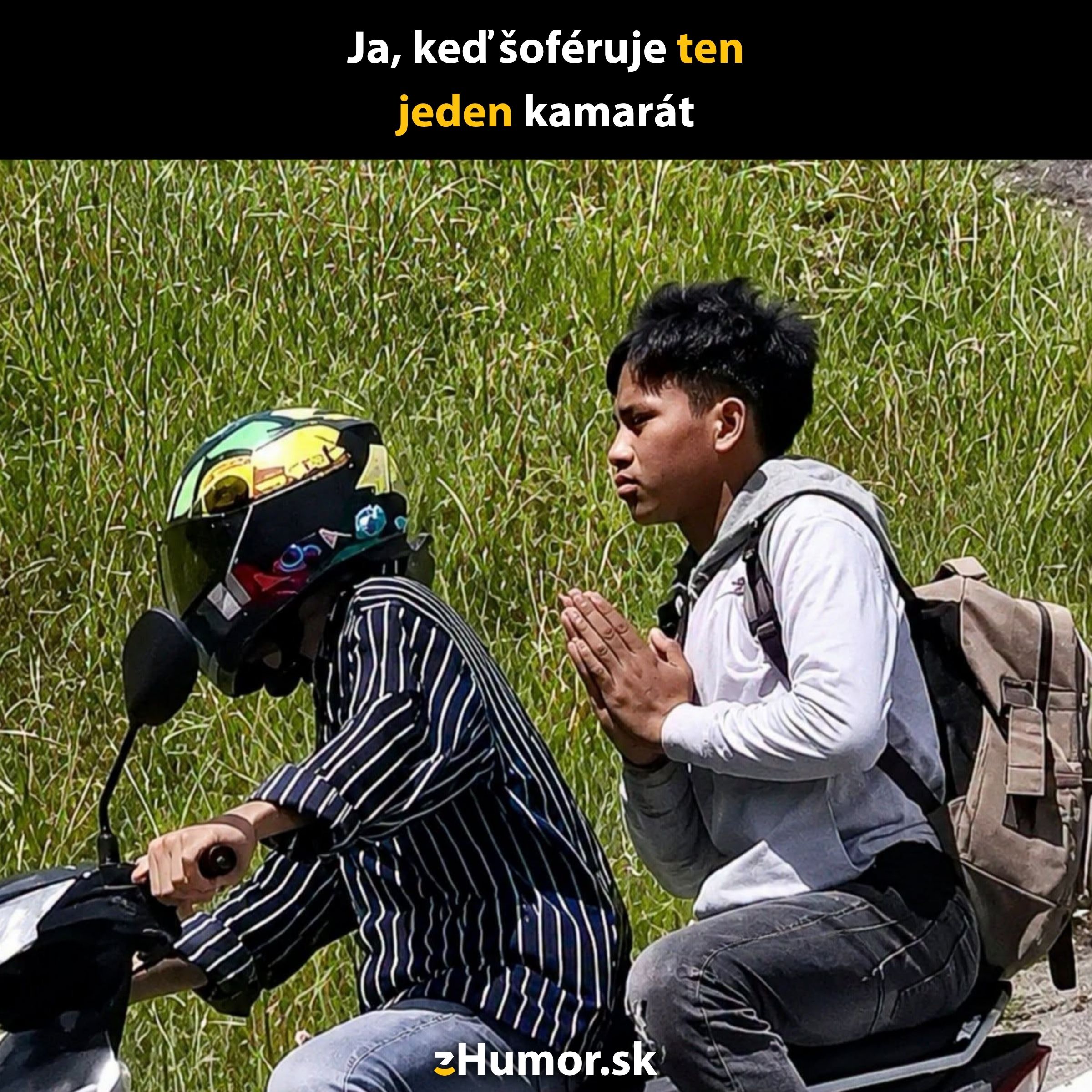 Motorkár s helmou a spolujazdec s rukami v modlitbe na pozadí trávy.