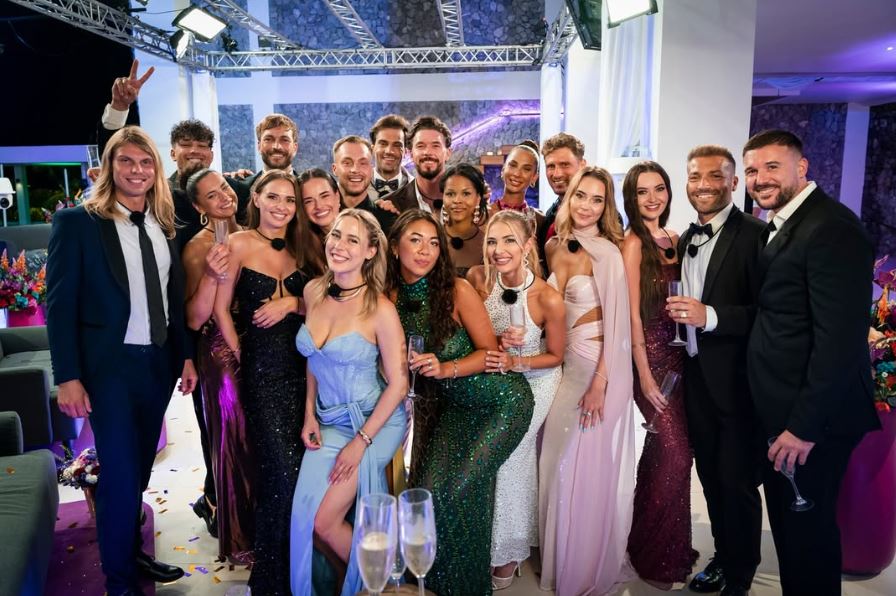 Skupina elegantne oblečených ľudí pózuje s pohármi na slávnostnom večierku plnom kvetinovej výzdoby.