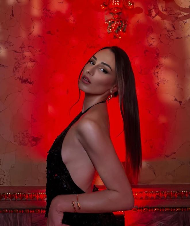 Žena v elegantných čiernych šatách pózuje pred červeným pozadím, pôsobivá atmosféra a vkusné osvetlenie.