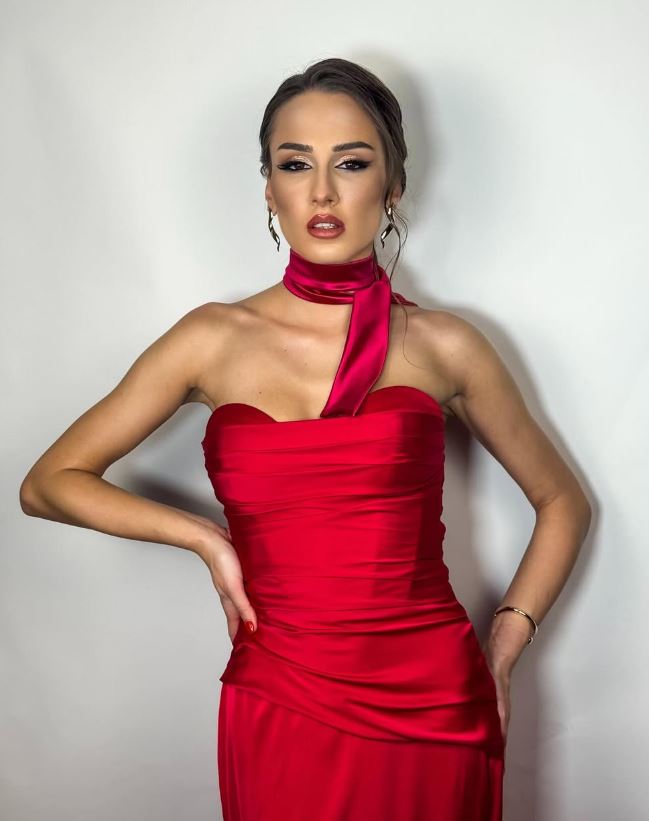 Osoba v červených večerných šatách pózuje na bielom pozadí, elegantný vzhľad a sofistikovaný štýl.