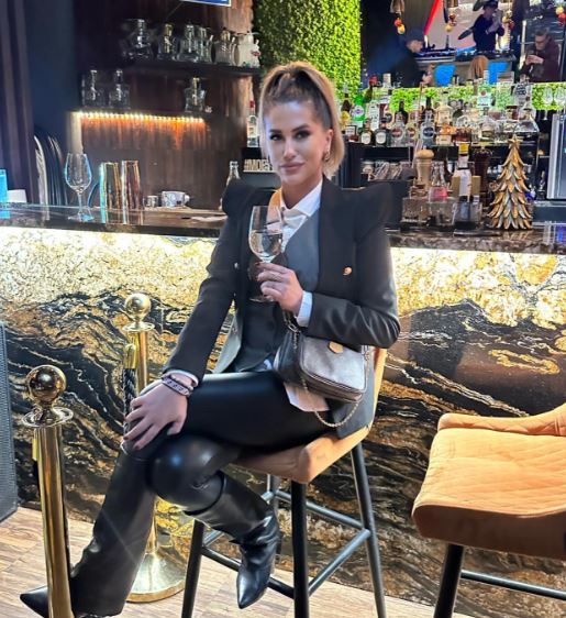 Osoba sediaca na barovej stoličke s pohárom v ruke, elegantný interiér, barový pult v pozadí.