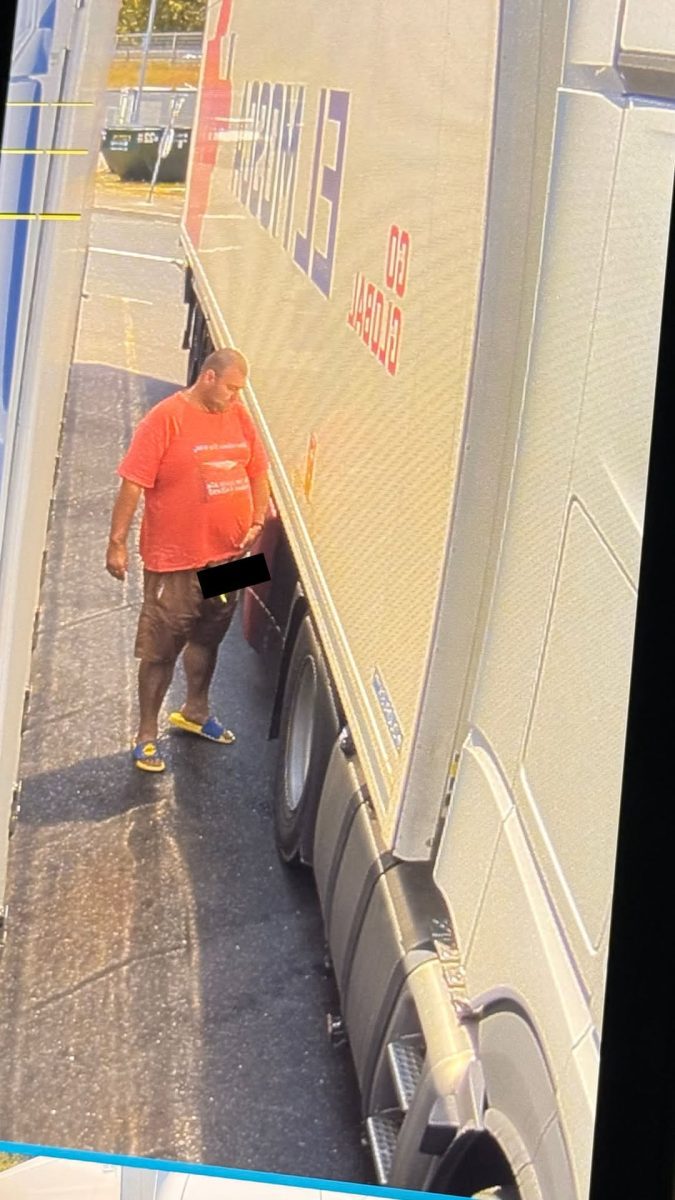 Osoba v červenom tričku stojí medzi dvomi nákladnými autami na parkovisku.