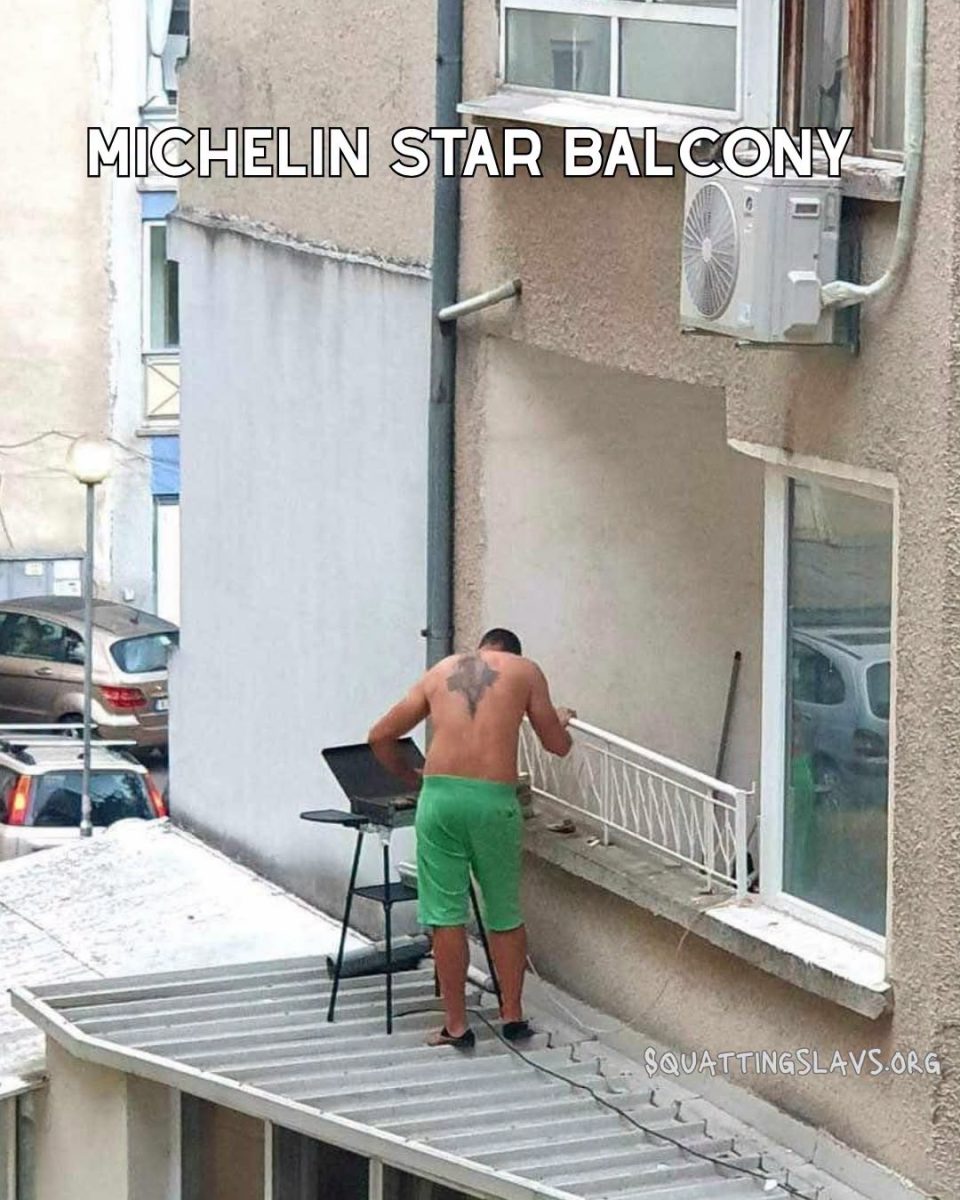 Muž v zelených šortkách griluje na balkóne, stojí na streche budovy.