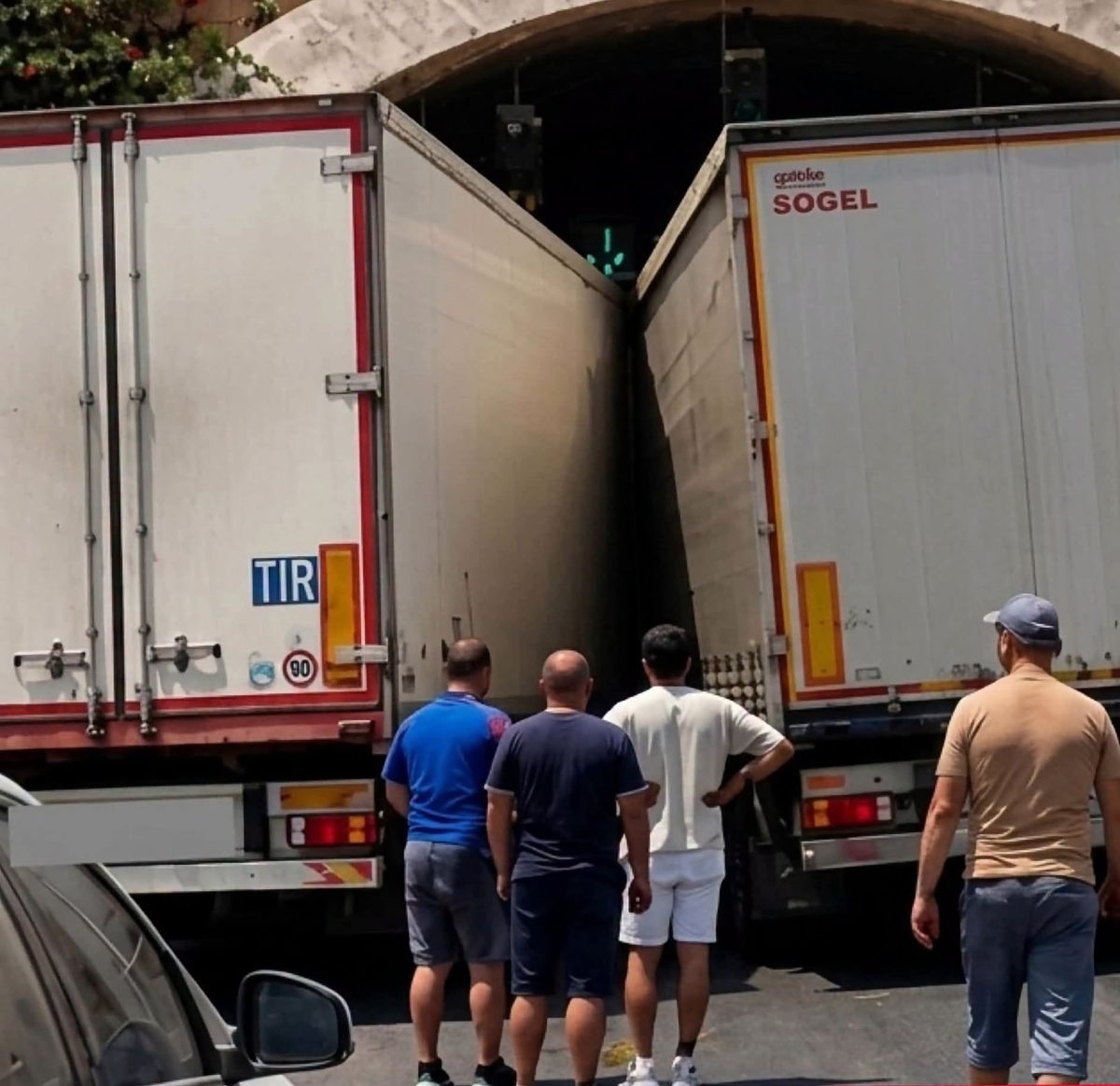 Dve kamióny zaseknuté v úzkom tuneli, štyria muži sledujú situáciu z predu.
