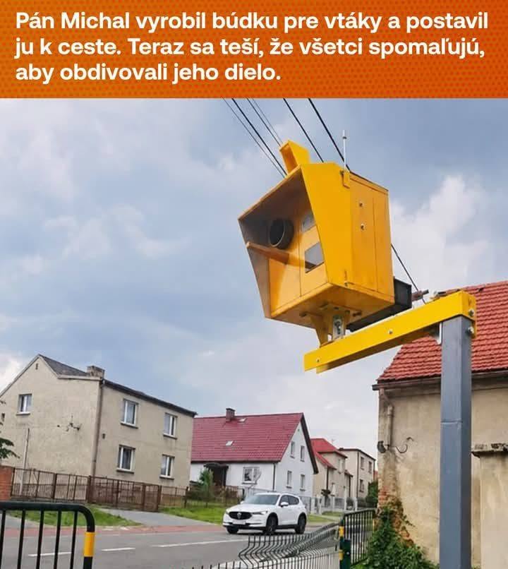 Žltá búdka pre vtáky vo forme rýchlostného radaru pri ceste, domy v pozadí. Kreatívne dielo priťahujúce pozornosť.