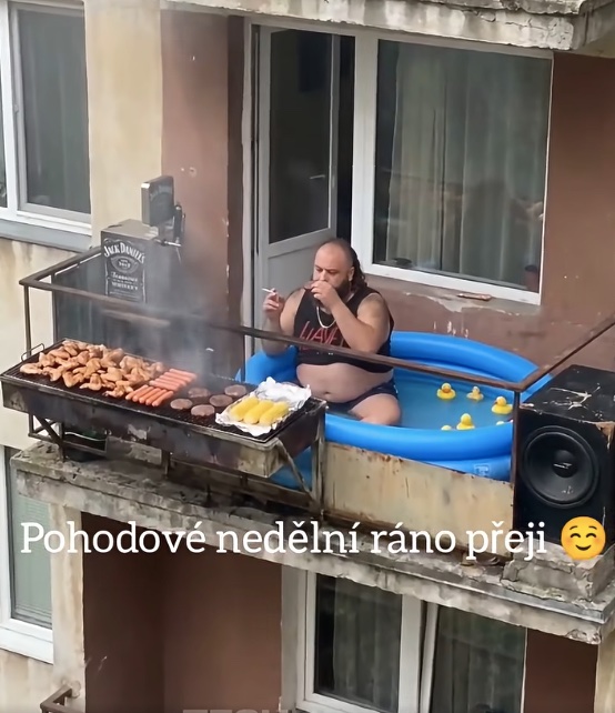 Muž relaxuje v bazéne na balkóne, griluje jedlo, obklopený gumovými kačkami, s nápisom „Pohodové nedělní ráno přeji“.