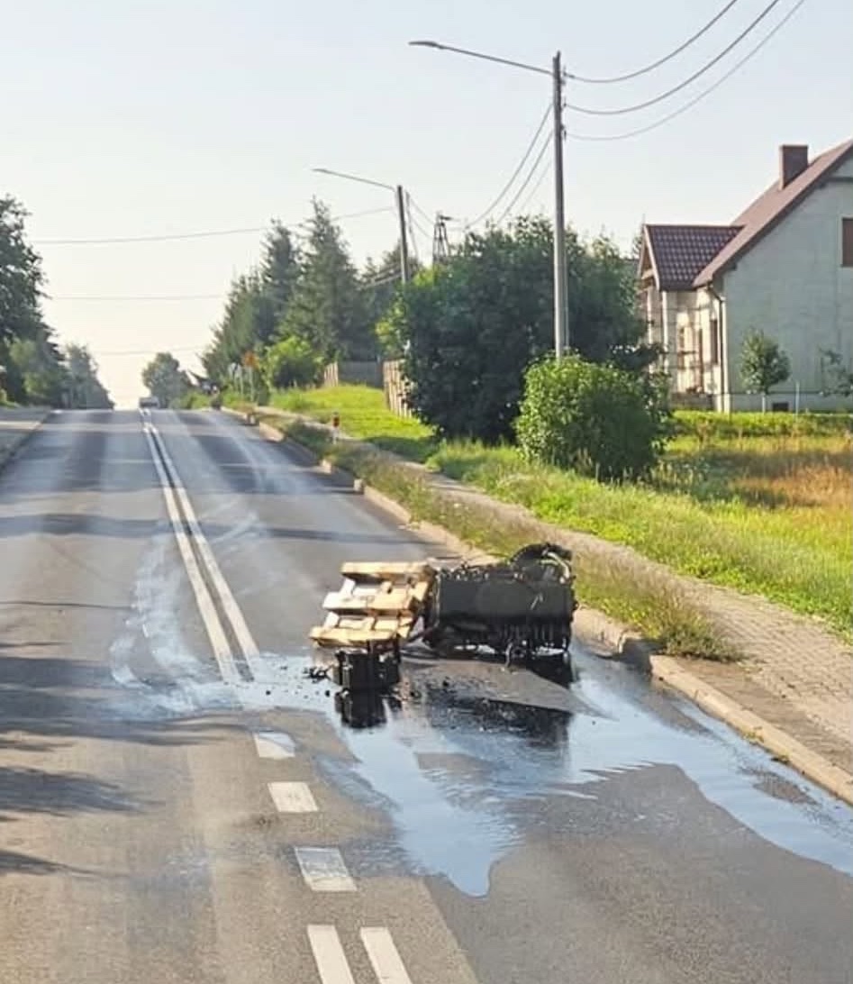 Rozliaty decht na ceste s prevráteným vozíkom, obytná štvrť, slnečný deň.