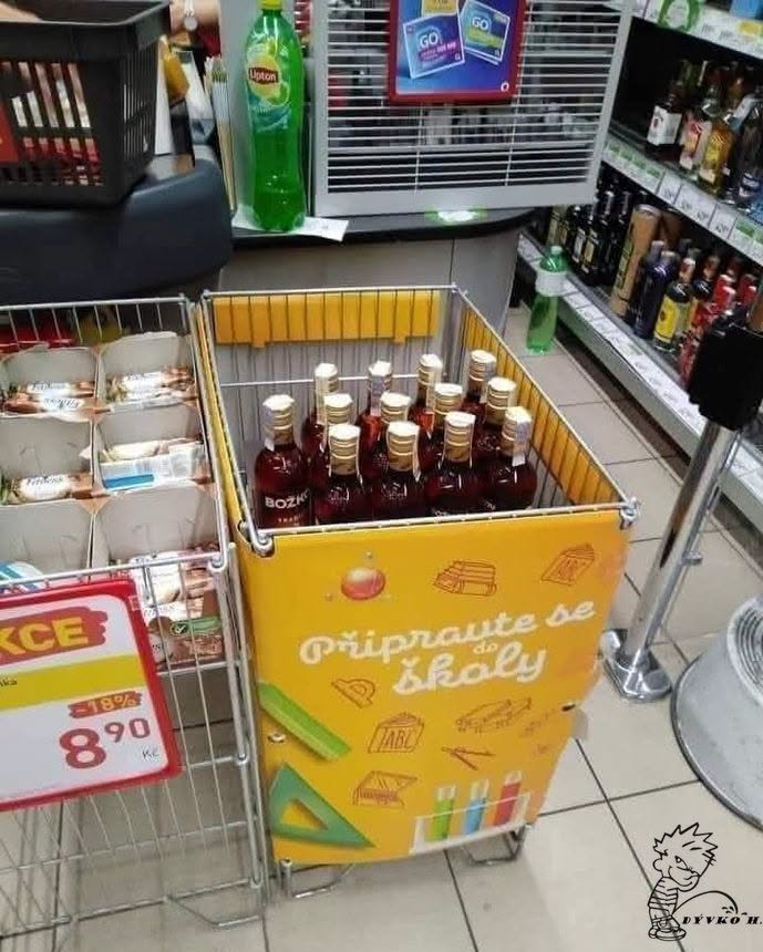 Košík s fľašami alkoholu s nápisom Pripravte se do školy v obchode, vedľa regálov s nápojmi a potravinami.