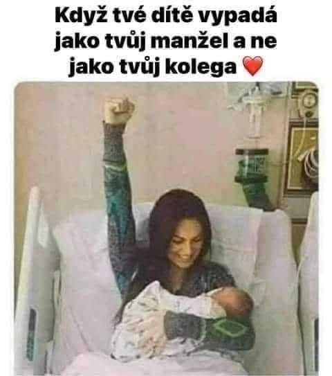 Žena v nemocnici radostne drží bábätko s úsmevom a zdvihnutou päsťou, šťastná z podoby svojho dieťaťa.