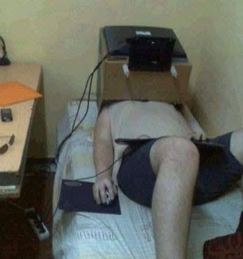 Osoba sledujúca televízor v ležiacej polohe s otvorenou škatuľou na hlave ako improvizovaným držiakom.