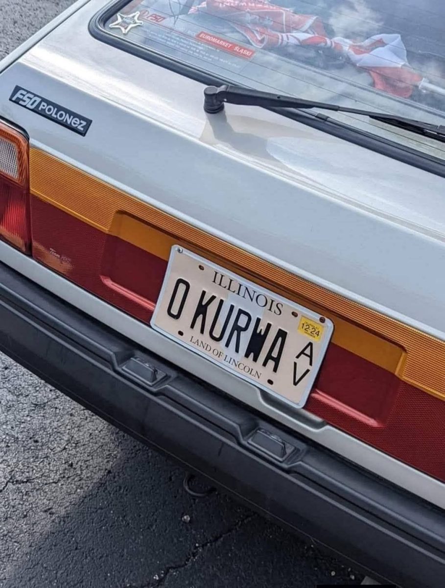 Retro auto s poznávacou značkou z Illinois a slovným vyhotovením O KURWA na parkovisku.