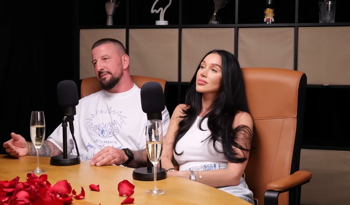 Pár sedí na podcastovom rozhovore, obklopení mikrofónmi a pohárikmi.