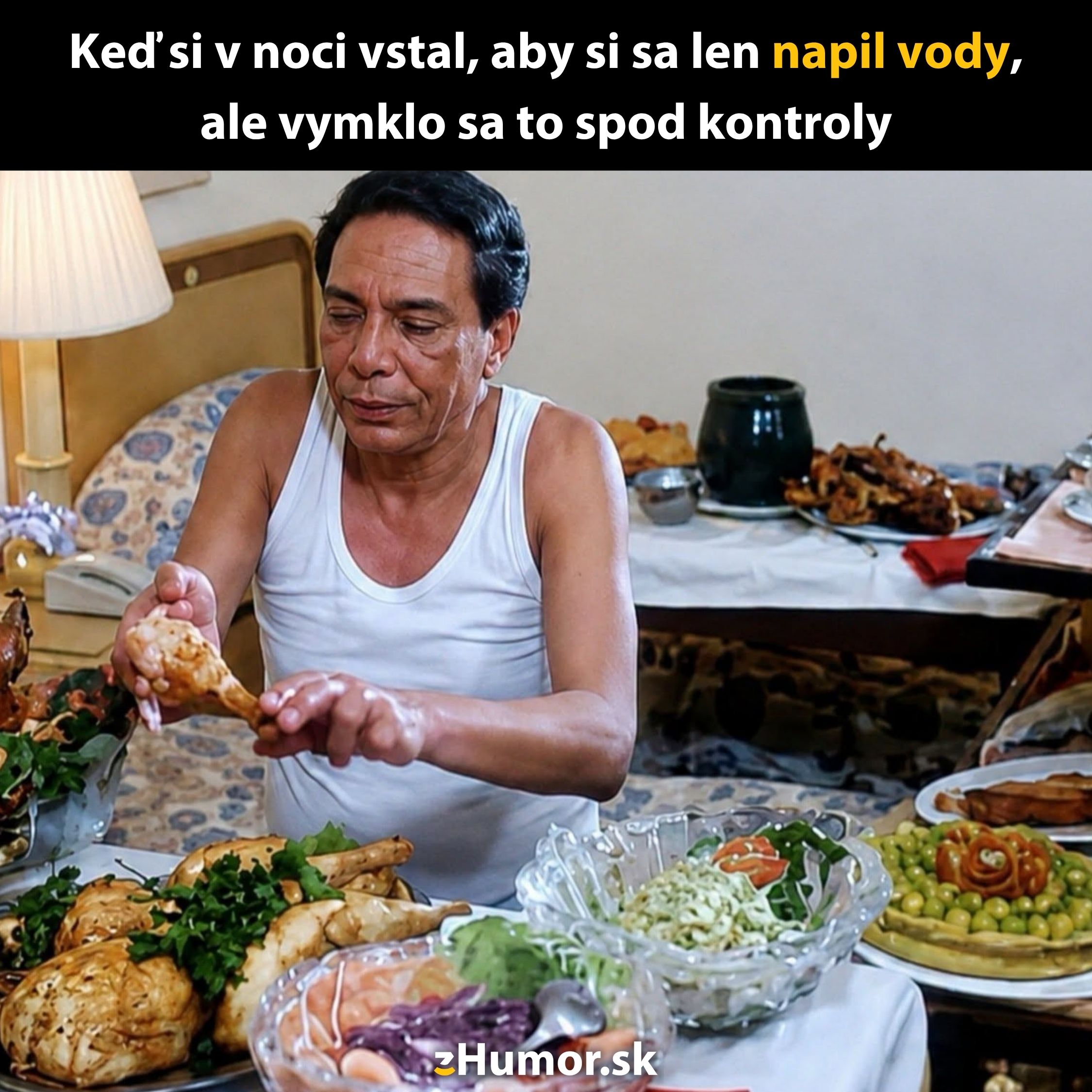 Muž sedí pri stole plnom jedla, obklopený mäsom a šalátmi v izbe. Je noc a jedlo je v popredí.