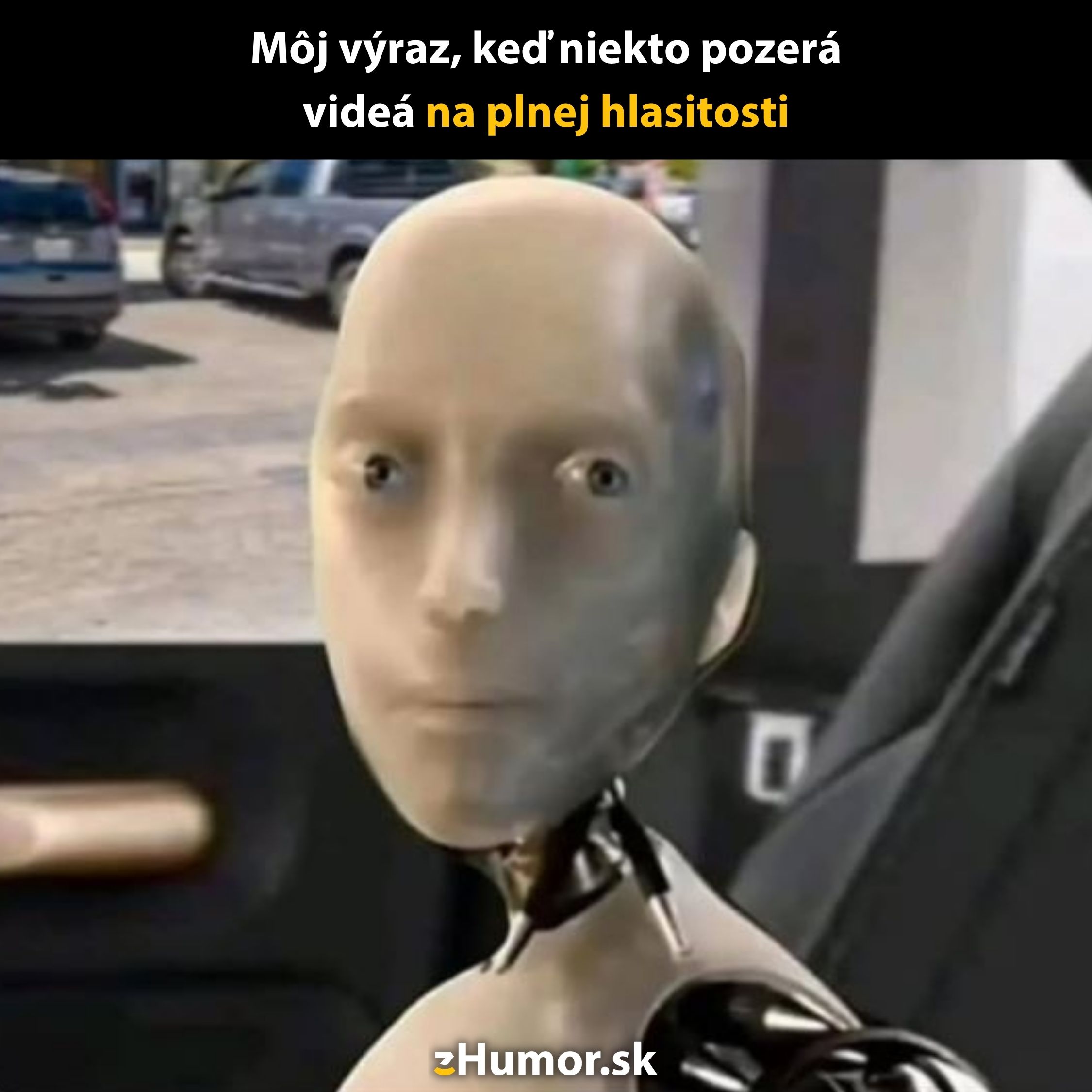 Robot s neutralným výrazom sediaci v aute. Text hore: Môj výraz, keď niekto pozerá videá na plnej hlasitosti.