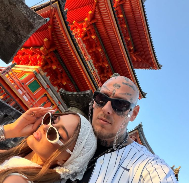 Pár v slnečných okuliaroch pózuje pred tradičnou japonskou architektúrou, živé farby chrámu a jasná obloha.