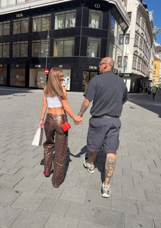 Pár sa prechádza po ulici pred luxusným obchodom Dior za slnečného dňa.