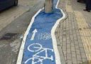 Modrý pruh so symbolom bicykla vedie okolo stĺpa na chodníku.