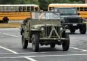 Historické vojenské vozidlo Jeep parkuje vedľa školských autobusov na parkovisku.