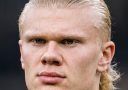 Blond muž s vážnym výrazom tváre a elegantným účesom, s vtipným textom o elektrotechnike v pozadí.